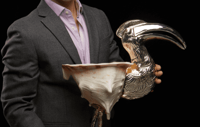 Auction specialist holding a polished silver toucan sculpture and a shell