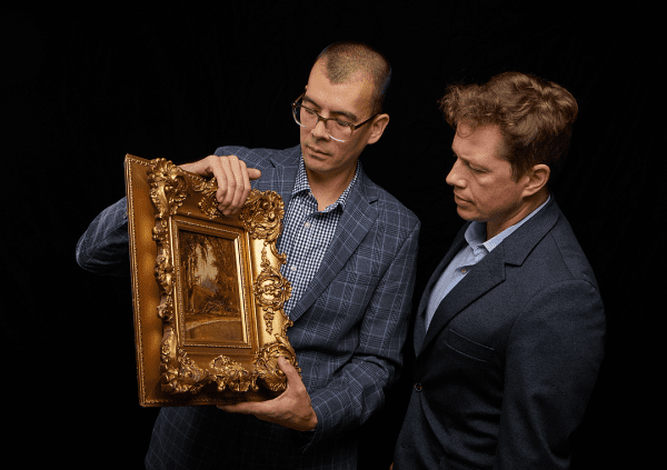 Two specialists examining a gilt-framed painting being considered for consignment