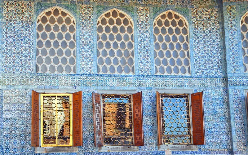 topkapi-palace-blue-porcelain-tile Facade of Topkapi Palace adorned with intricate blue and white porcelain tiles and shuttered windows.